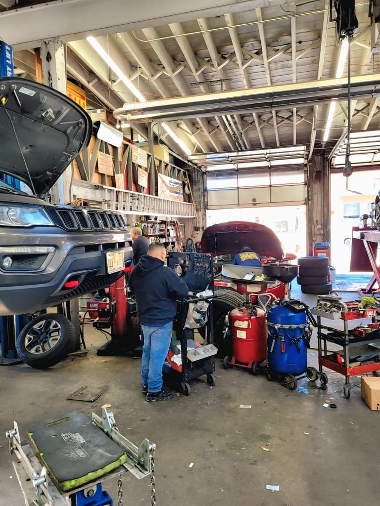 Mechanic working on a vehicle in a spacious auto repair garage with multiple cars, tools, and equipment