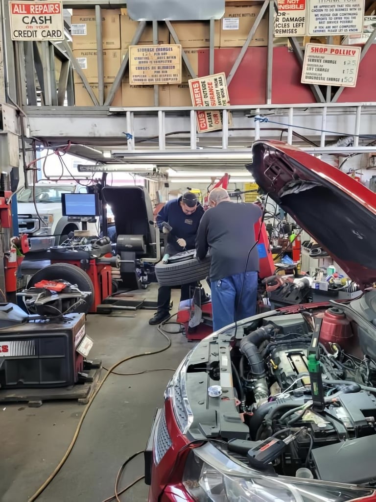 Mechanic working on a red car engine in a busy auto repair shop with tools and equipment visible