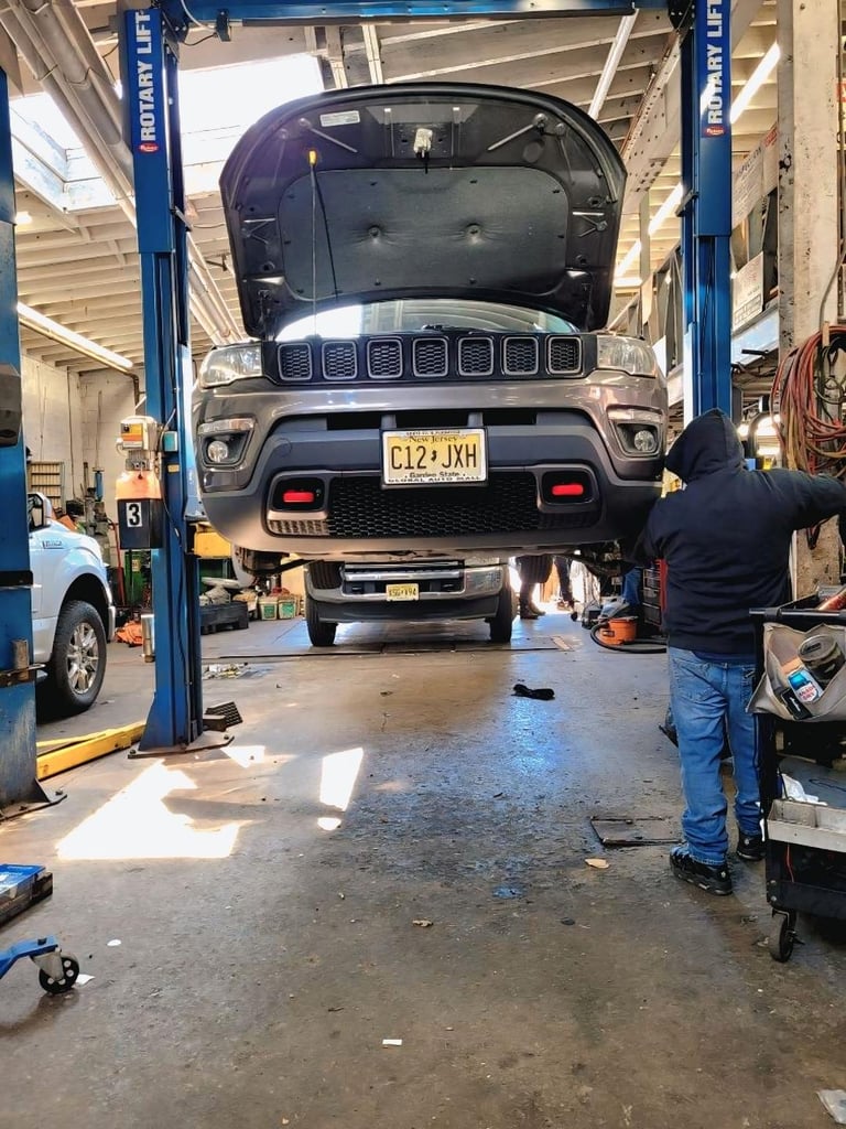 Dark SUV lifted on blue hydraulic car lift in auto repair shop with mechanic working nearby