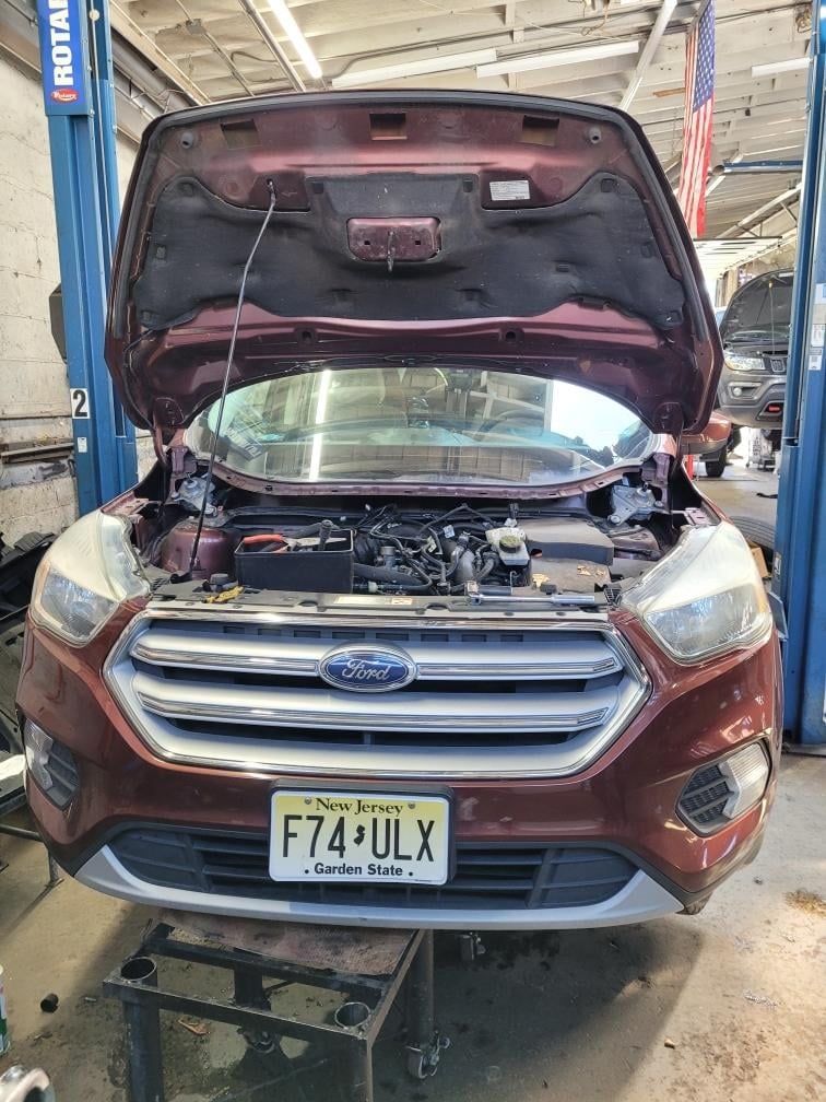 Red Ford vehicle with open hood displayed in a service bay at an auto repair shop with lift equipment